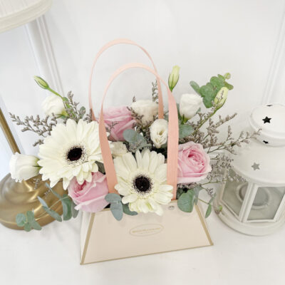 handbag design flower arrangement with pink roses, white gerberas, white eustoma, and greenery in soft pastel tones