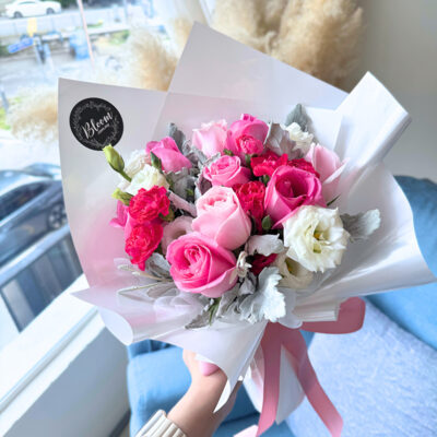 flower bouquet featuring hot pink and pink roses with white eustoma and cherry pink carnations wrapped in white paper with pink ribbon