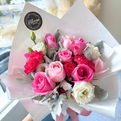 a bouquet of mixed flowers including hot pink roses, pink roses, white eustoma, and cherry pink carnations wrapped in translucent white paper