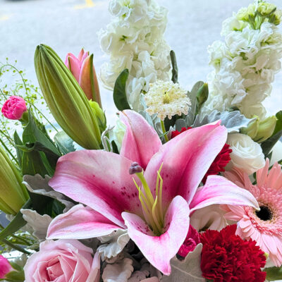 a floral box arrangement with pink roses, red carnations, stargazer lilies, and delicate white flowers