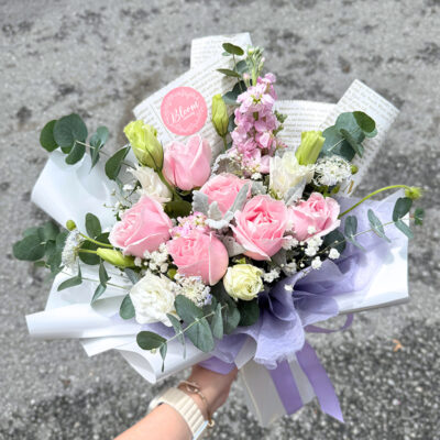flower bouquet featuring pink roses, white eustoma, matthiola, and baby's breath wrapped in white and purple paper
