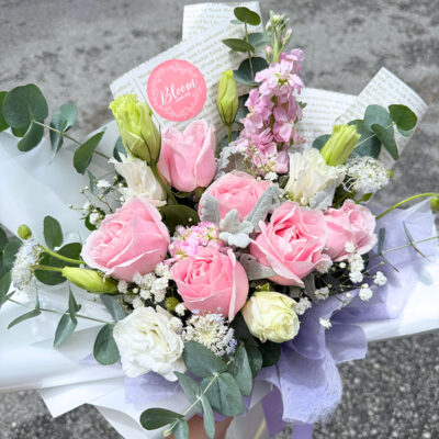 a bouquet of pink rose blooms mixed with white eustoma, matthiola, and delicate baby's breath in soft wrapping