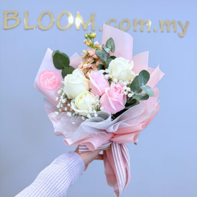 hand bouquet with white and pink roses, matthiola, and baby's breath wrapped in soft pink paper