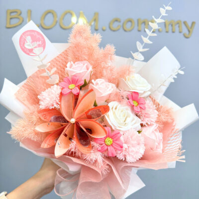 a bouquet of pink soap roses, white soap roses, and pink soap carnations combined with cash flower elements and wrapped in layered pink and white sheets.