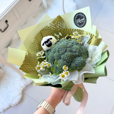 a mothers day flower bouquet wrapped in green paper featuring fresh broccoli, chamomile flowers and a small sheep decoration