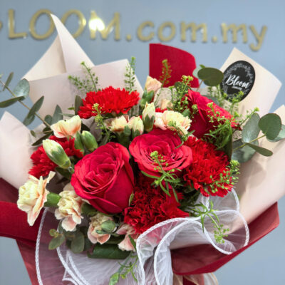 a bouquet of mixed red roses and carnations accented with soft carnation sprays and wrapped in layered papers with white lace trim.