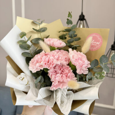 a bouquet of imported pink carnations accented with bunny tail and eucalyptus leaves in layered white and gold wrapping