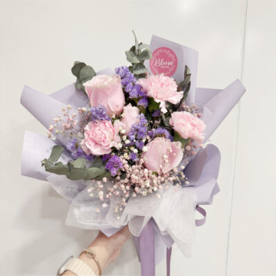 hand bouquet with pink carnation and pink rose flowers accented by coloured baby's breath and statice wrapped in lilac paper