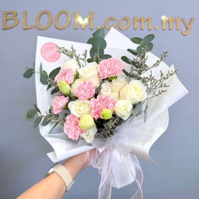 a mother's day flower bouquet featuring pink carnations, white roses, white eustoma, and caspia wrapped in white paper with greenery