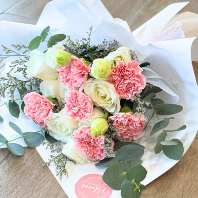 wrapped bouquet of mixed pink carnations and white roses accented with eustoma and caspia greenery