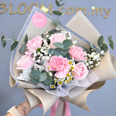 mothers day hand bouquet with pink roses and carnations accented by baby's breath and chamomile, wrapped in layered neutral-toned paper with a pink ribbon