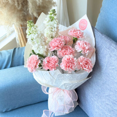 a flower bouquet wrapped in white paper featuring pink carnation and white matthiola with a soft pink ribbon