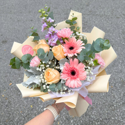 flower bouquet with pink gerbera, champagne rose, pink carnation, matthiola, and babyโs breath wrapped in cream paper