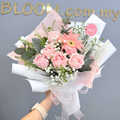 flower bouquet of five pink roses with a pink gerbera and baby's breath wrapped in white and soft pink paper
