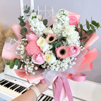 a flower bouquet featuring pink roses, white roses, pink gerbera, and eucalyptus wrapped in soft pink paper with a ribbon