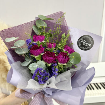 flower bouquet featuring six imported purple carnations with greenery and purple accents wrapped in layered lilac paper