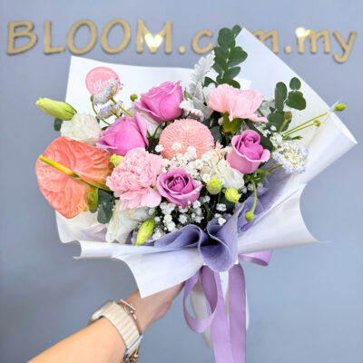 flower bouquet featuring purple roses with pink carnation, pink anthurium, and white eustoma wrapped in lavender colour paper.