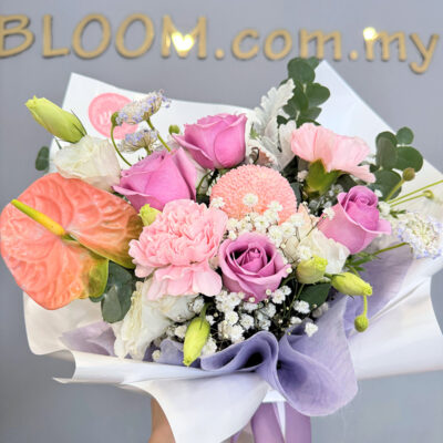 a bouquet of mixed flowers including purple roses, pink chrysanthemum pingpong, and babyโs breath with soft greenery in a layered wrap.