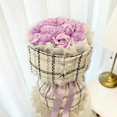 flower bouquet of purple soap carnations and roses wrapped in checked fabric with purple ribbon accent.