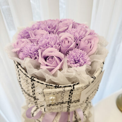 a bouquet featuring purple soap roses and carnations arranged elegantly with soft white tissue and textured wrap.