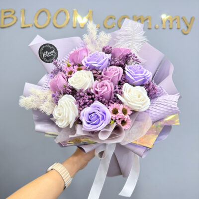 a flower bouquet featuring purple and white soap roses with soap chamomile and preserved baby's breath wrapped in lilac paper