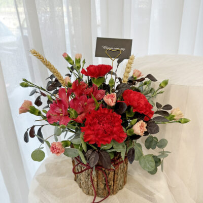 flower arrangement in a rustic bark barrel featuring red carnations, alstroemeria, and pink carnation spray with green and dark foliage