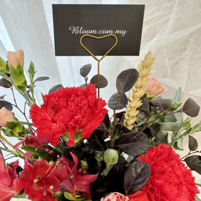 a flower arrangement in a bark-textured bucket with vibrant red carnations, soft pink carnation spray, and alstroemeria blooms