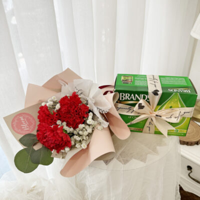 a bouquet of three red carnations with white baby's breath wrapped in soft pink paper