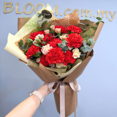 hand bouquet with red carnation stalks and peach carnation spray wrapped in brown and cream textured paper