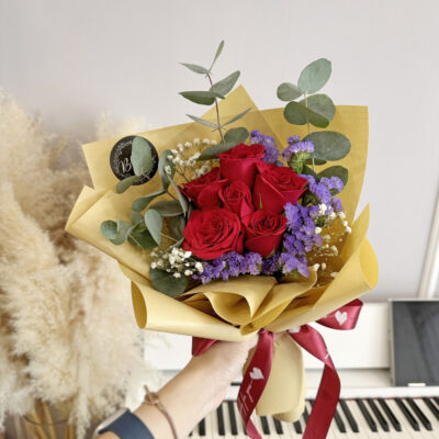 flower bouquet with 6 red roses wrapped in beige paper, accented with purple statice, white baby's breath, and eucalyptus leaves