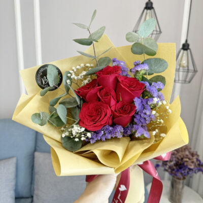 a bouquet featuring vibrant red roses combined with purple statice and delicate baby's breath, wrapped in beige textured paper