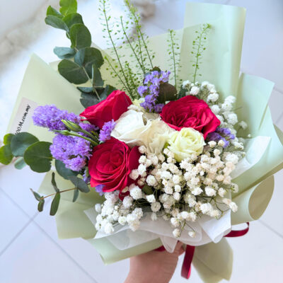 flower bouquet with three red roses, white eustoma, purple statice, and baby's breath wrapped in soft green paper
