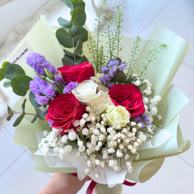 a bouquet featuring red roses, white eustoma, statice, and baby's breath with greenery wrapped in pale green paper