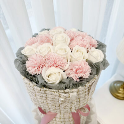 a bouquet of mixed pink soap carnations and white soap roses arranged in a soft fabric wrap tied with a pink bow