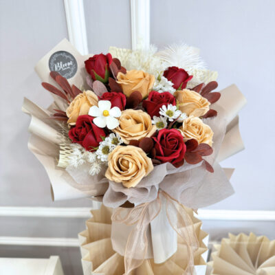 a flower bouquet featuring red and milktea soap roses with soap chamomile and dried violet flowers wrapped in cream paper
